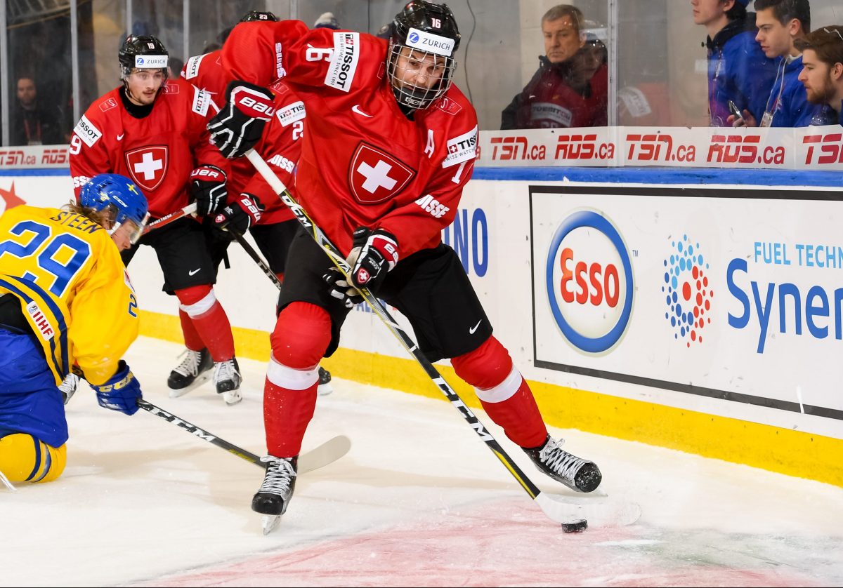 BUFFALO, NEW YORK - DECEMBER 30: Switzerland's Nico Gross #16 controls the puck against Sweden during the preliminary round of the 2018 IIHF World Junior Championship. (Photo by Andrea Cardin/HHOF-IIHF Images)