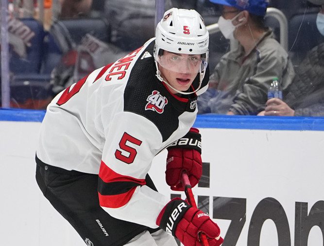 New Jersey Devils defenseman Luke Hughes, right, sits on the bench